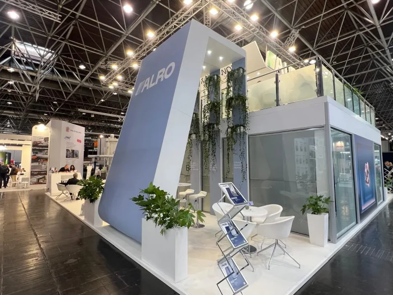 Glass-walled meeting rooms under the upper deck of the ALRO stand at ALUMINIUM 2026